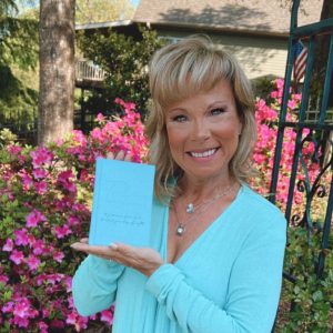 Dr. Michelle Bengtson holding a copy of the book, Today is Going to be a Good Day, standing in front of a flower garden.